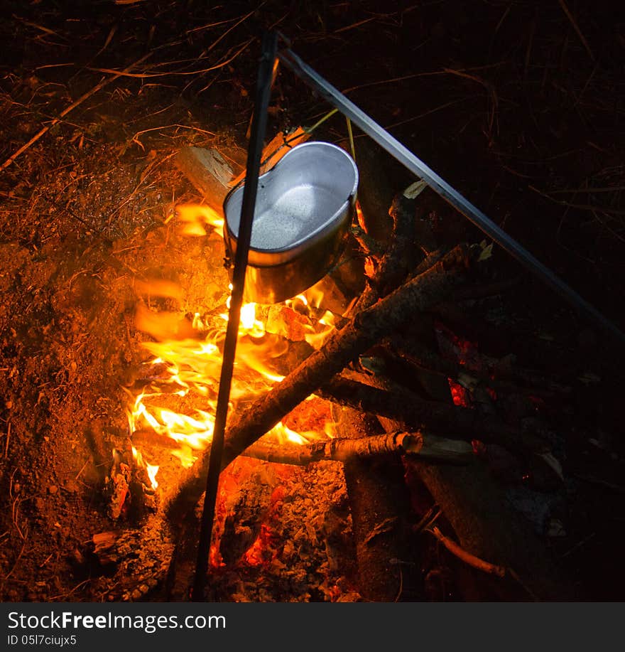 Water begins to boil in a kettle on a fire in the night. Water begins to boil in a kettle on a fire in the night