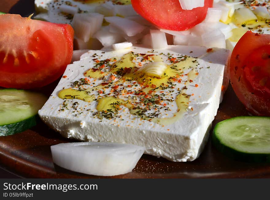 Feta cheese cut in slices, with fresh vegetables, dry herb spices and olive oil - the ingredients for a healthy greek salad. Feta cheese cut in slices, with fresh vegetables, dry herb spices and olive oil - the ingredients for a healthy greek salad