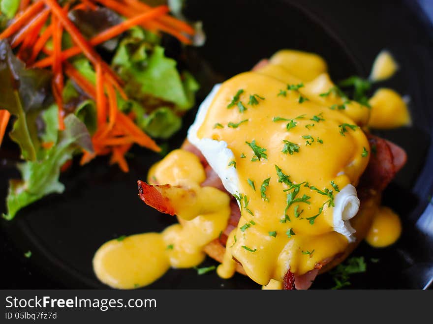 Eggs benedict with salad and bacon in dishes black