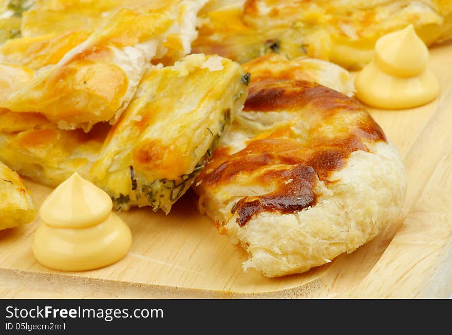 Slices of Cheese and Greens Puff Pastry Pie Garnished with Cheese Sauce closeup on Cutting Board. Slices of Cheese and Greens Puff Pastry Pie Garnished with Cheese Sauce closeup on Cutting Board