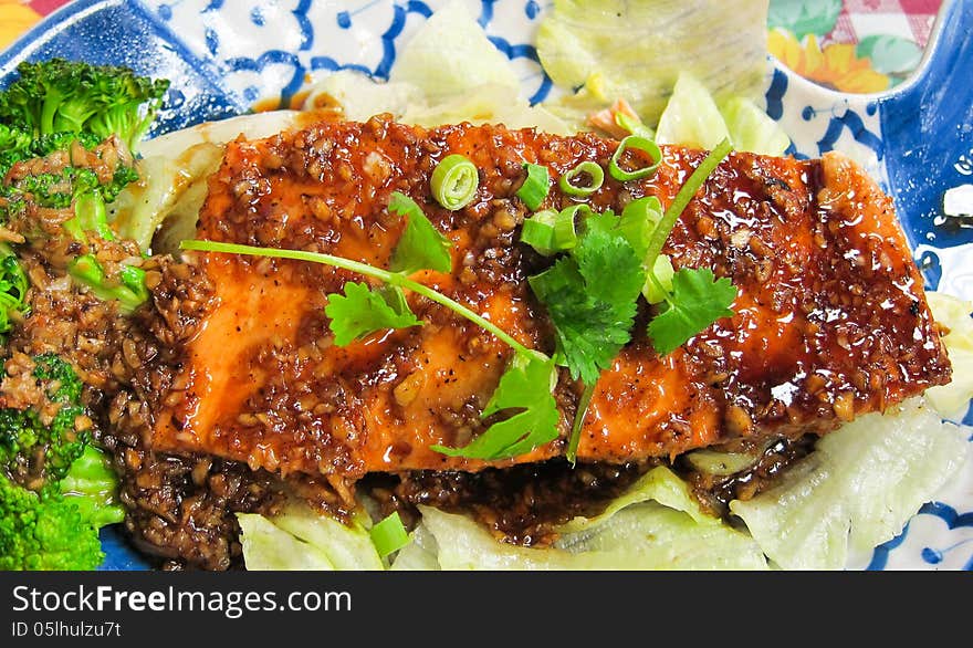 A baked salmon fillet with garlic sauce settled on a bed of lettuce. Thai cuisine.