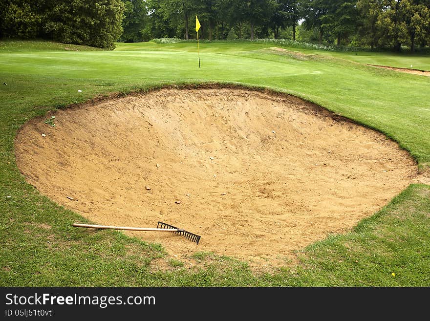 Rake lying in bunker on edge of green on gold course. Rake lying in bunker on edge of green on gold course