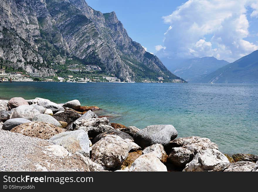 Image shows Limone on the left, Lake Garda in the middle, some mountains on both sides and stony beach in the front. Image shows Limone on the left, Lake Garda in the middle, some mountains on both sides and stony beach in the front.