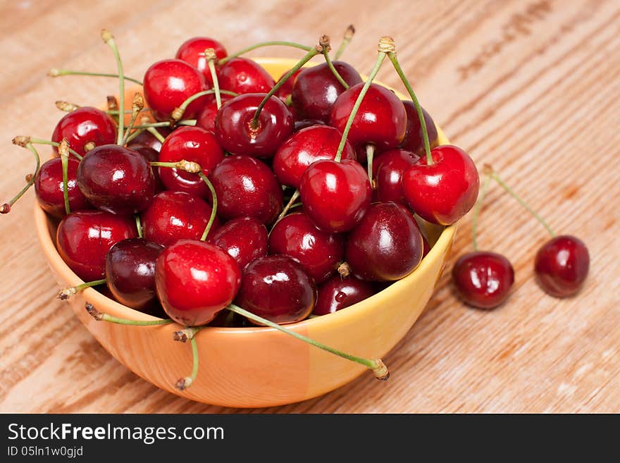 Ripe cherries in a yellow bowl on wooden table