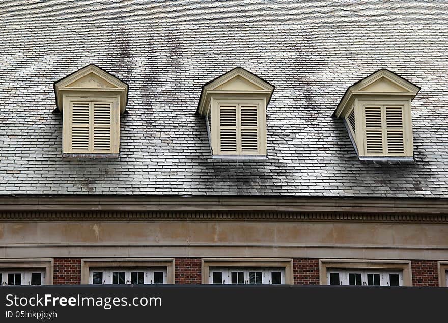 Three shuttered windows on roof of red brick building.