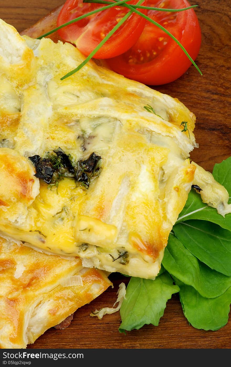 Slices of Cheese and Greens Pie Garnished with Tomatoes, Spring Onion and Basil on Wooden Plate closeup