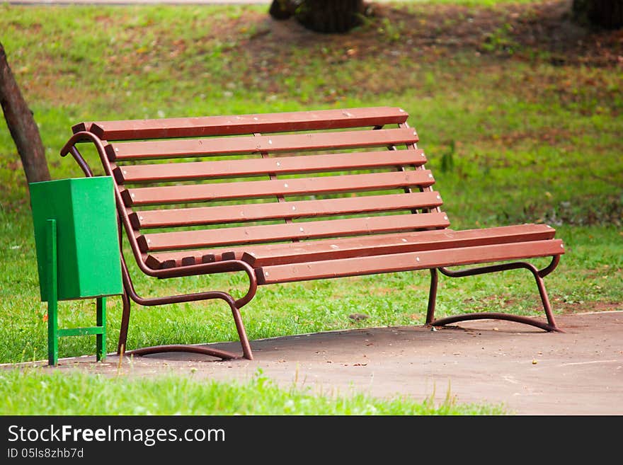 Old brown wooden bench in the park on a background of green grass in the shadow. Old brown wooden bench in the park on a background of green grass in the shadow