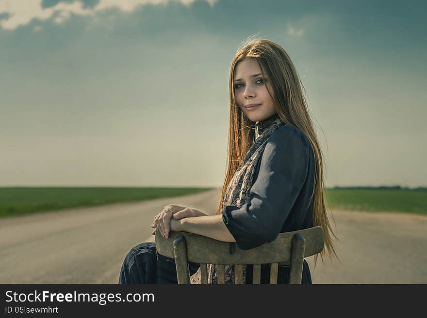 Beautiful girl with long hair sits outdoors on a chair on the road