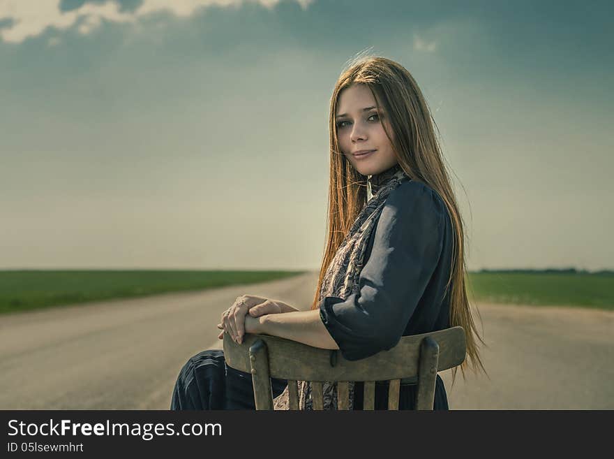 Beautiful Girl With Long Hair Sits Outdoors On A Chair On The Road