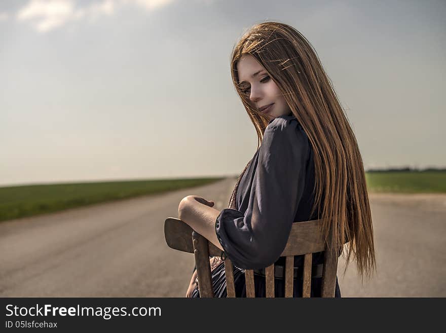 Beautiful girl with long hair sits outdoors on a chair on the road