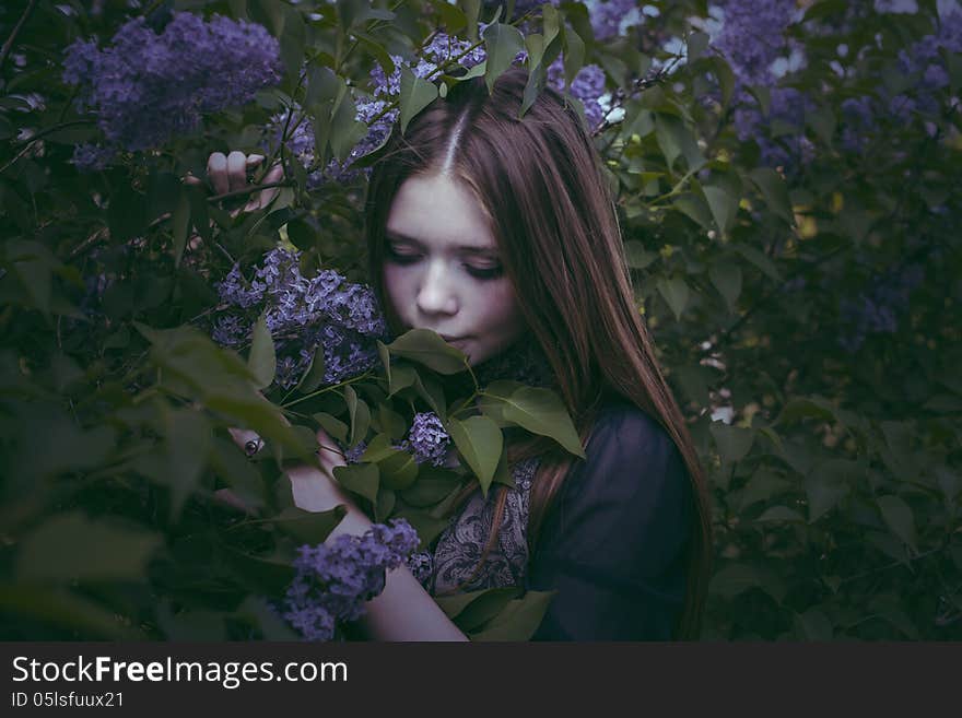 Beauty young girl in fashion style smells lilac flowers outdoors