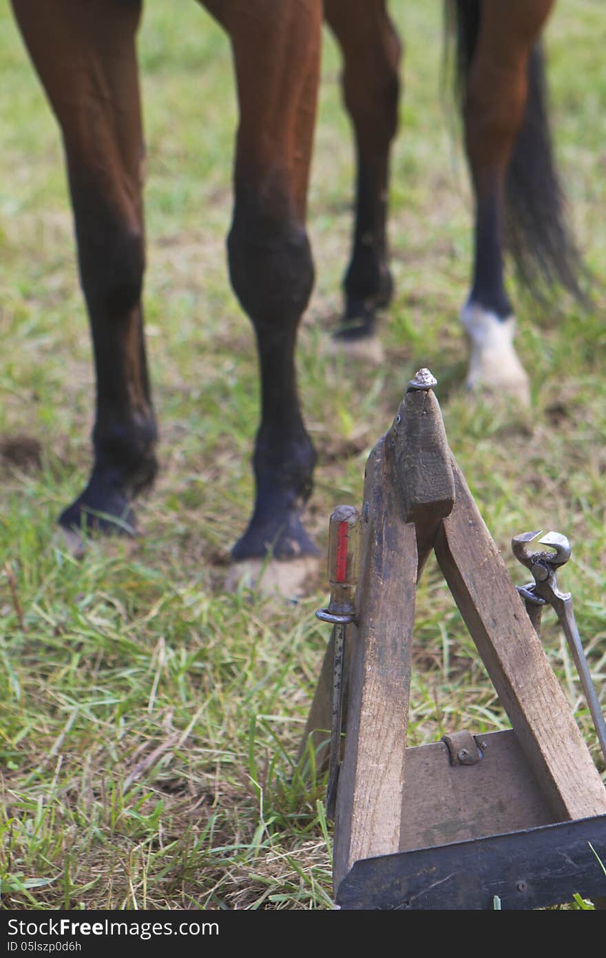 A farrier's hoof stand, tools attached, with a horse standing in the background. A farrier's hoof stand, tools attached, with a horse standing in the background.