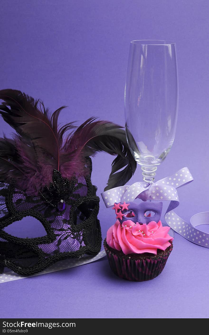 Pink and purple masquerade masks decorated party cupcake with pink frosting for teenage, birthday, New Years Eve, or wedding bridal shower party - with champagne glass and mask, vertical. Pink and purple masquerade masks decorated party cupcake with pink frosting for teenage, birthday, New Years Eve, or wedding bridal shower party - with champagne glass and mask, vertical.