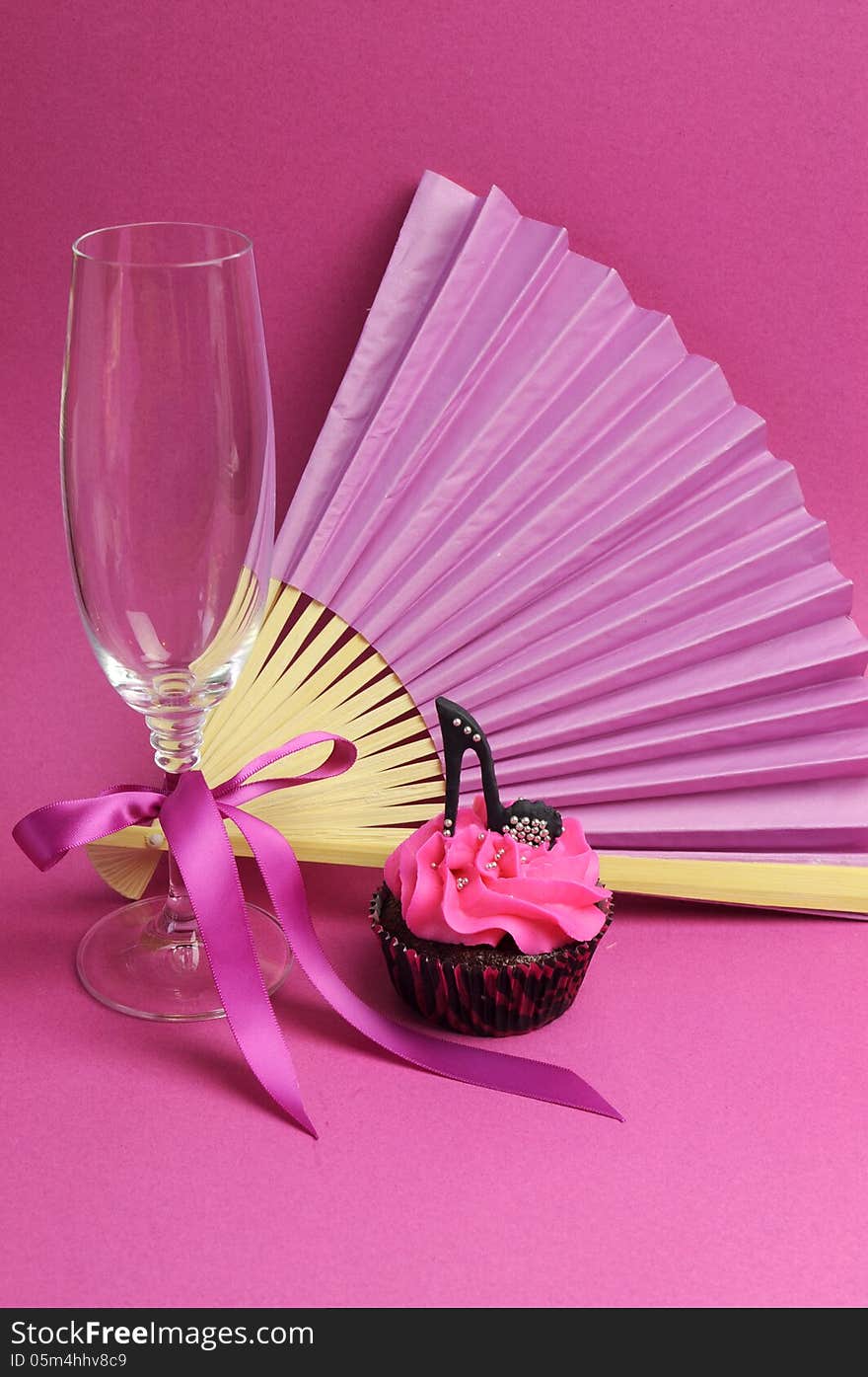 Pink party decorations with fan, champagne glass and high heel shoe cupcake - vertical.