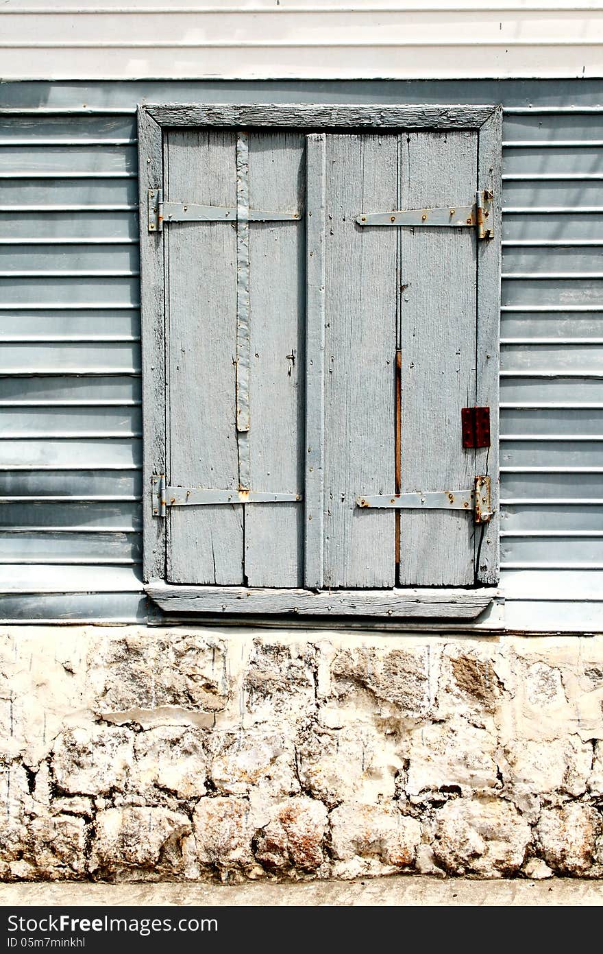 Image of an old window with wooden shutters set in a wall of stone and corrugated iron sheets. Image of an old window with wooden shutters set in a wall of stone and corrugated iron sheets