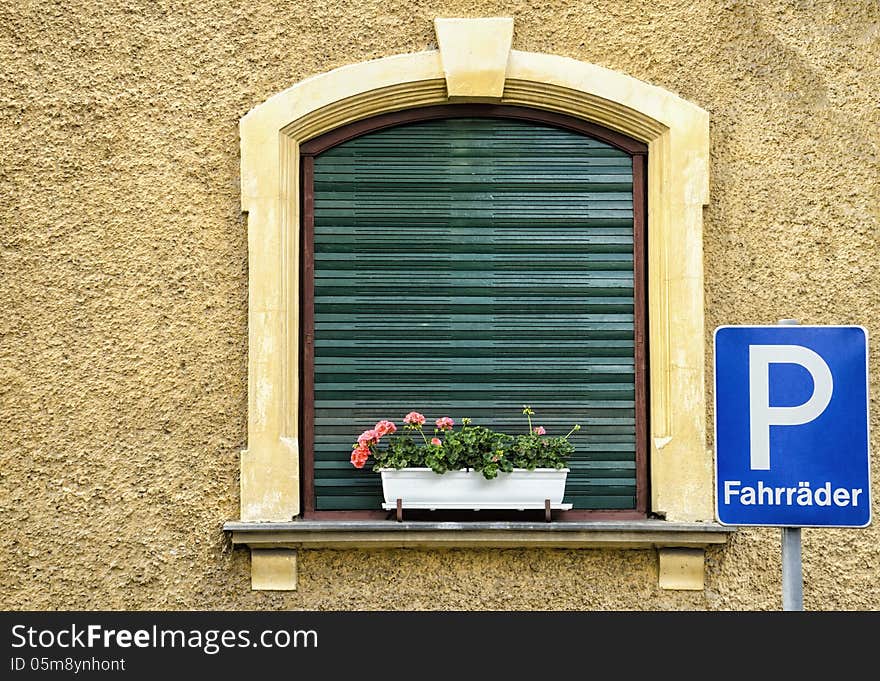 An European window with flowers and a bike parking board.