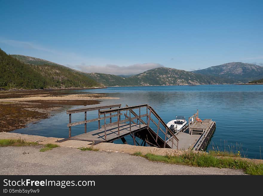 Quay by a fjord in Norway with small motorboat by a pier. Quay by a fjord in Norway with small motorboat by a pier.