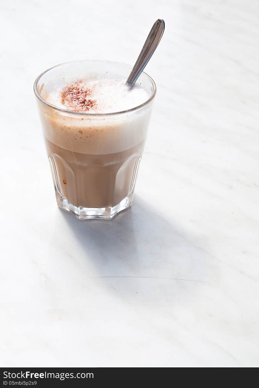 Coffee glass with spoon on a marble table outdoors.