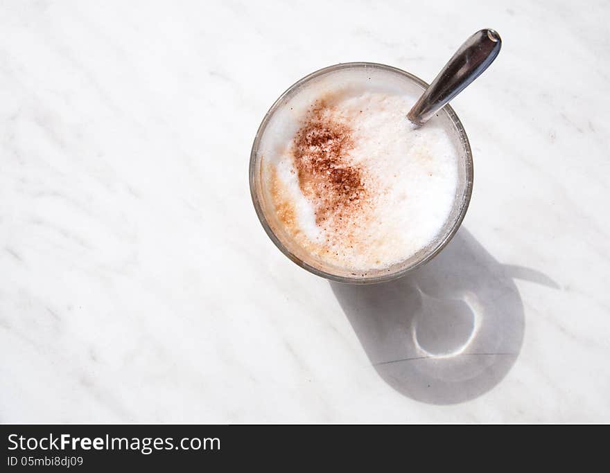 Coffee glass with spoon on a marble table outdoors, seen from above. Coffee glass with spoon on a marble table outdoors, seen from above.