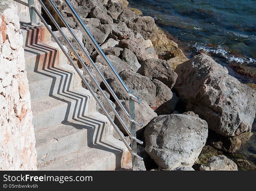 Stairs by the Mediterranean sea with rocks and zigzag shadow pattern. Mallorca, Balearic islands, Spain.