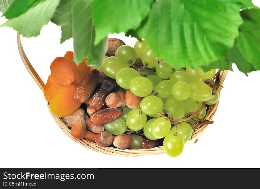 Dried fruits an grapes in a basket under foliage on white background. Dried fruits an grapes in a basket under foliage on white background