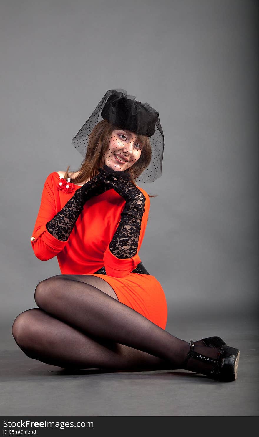 Young girl in a red dress and a black hat with a veil sitting on the floor