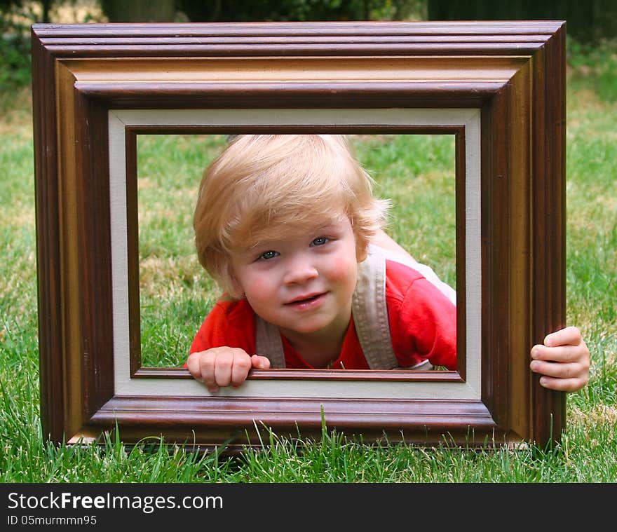 Cute little toddler boy laying on a lawn looking through a wooden frame. Cute little toddler boy laying on a lawn looking through a wooden frame.