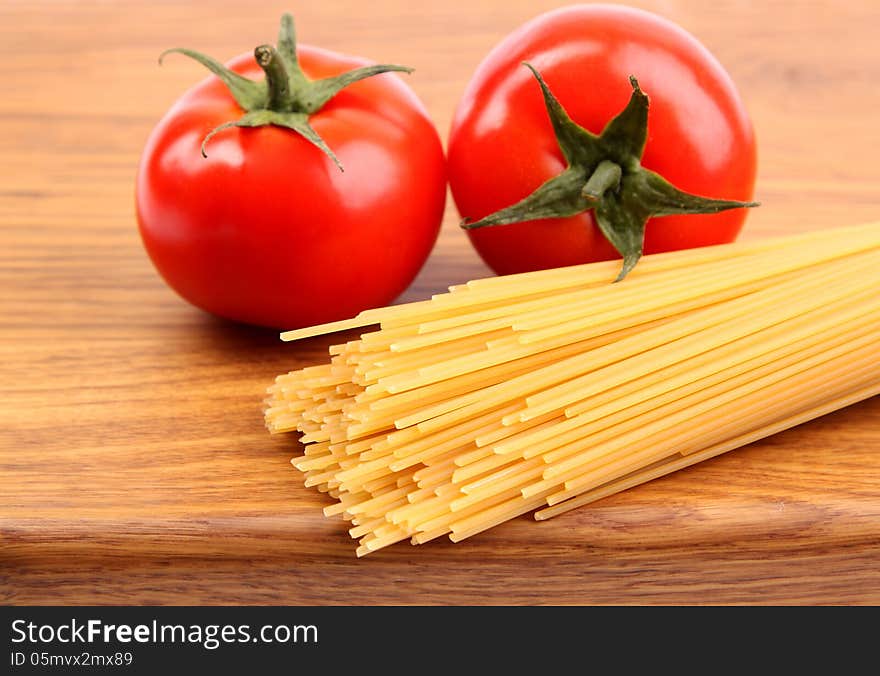 Tomatoesl and uncooked spaghetti on a cutting board close-up