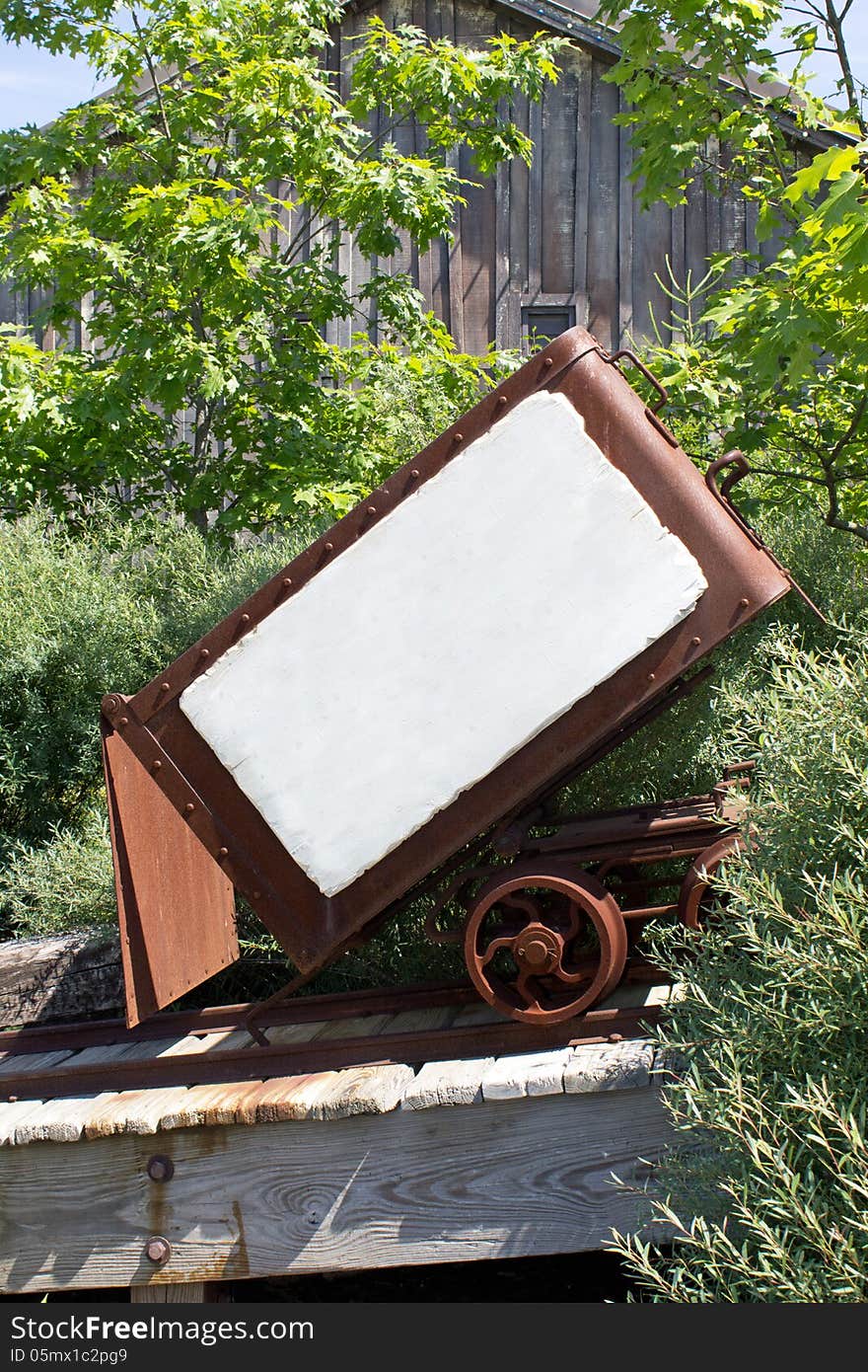 An open mining cart with a whiteboard on the side and a cabin in the background. An open mining cart with a whiteboard on the side and a cabin in the background