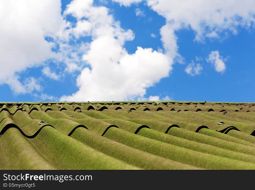 White clouds in blue sky above roof of house