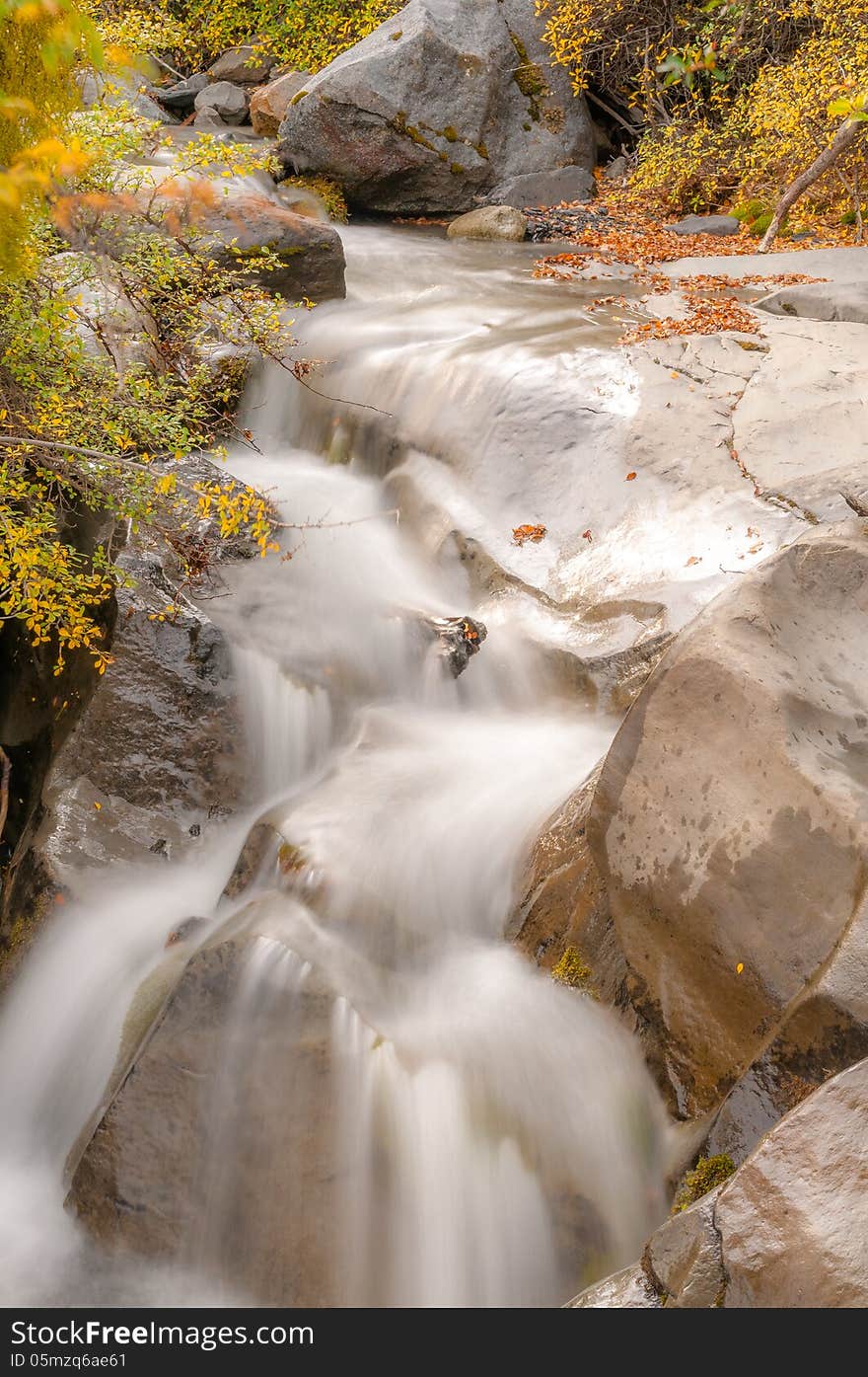 Clear water waterfall in autumn between rocks and orange and yellow leaves