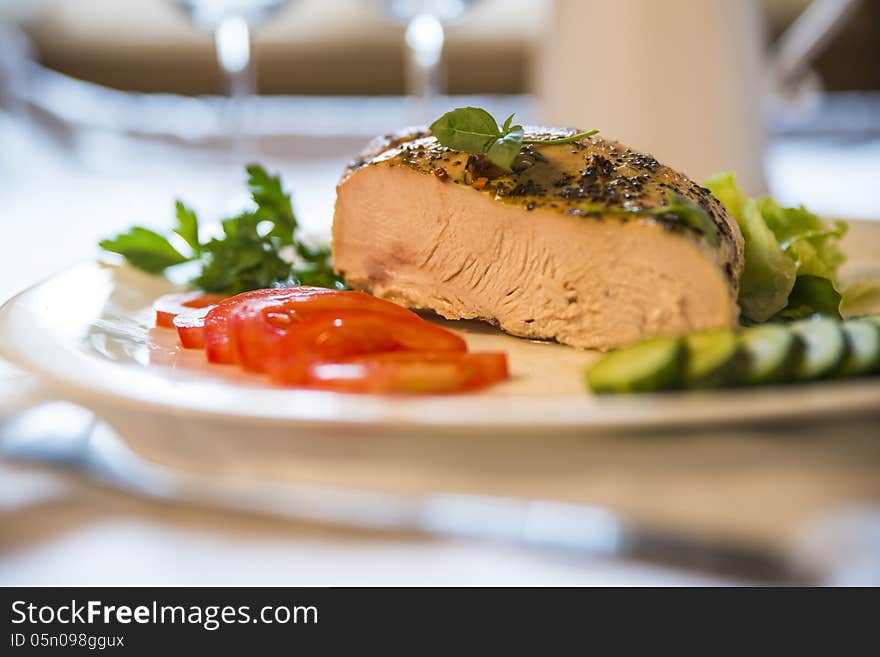 Fried peppery meat with spices and basil on top, served on a white plate with fresh tomatoes and cucumbers. Blurred background. Selective focus. Fried peppery meat with spices and basil on top, served on a white plate with fresh tomatoes and cucumbers. Blurred background. Selective focus.