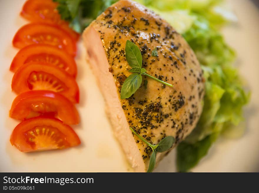 Fried peppery turkey meat with spices and basil on top, served on a white plate with fresh tomatoes and green salad. Blurred background. Selective focus. Fried peppery turkey meat with spices and basil on top, served on a white plate with fresh tomatoes and green salad. Blurred background. Selective focus.