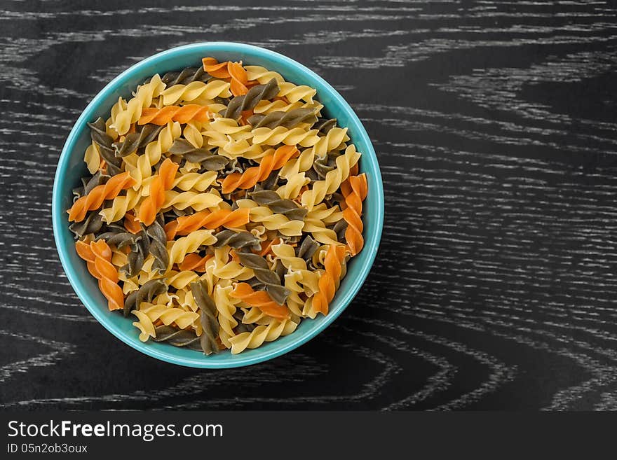 Colorful raw fusilli in blue bowl on black wood table. Colorful raw fusilli in blue bowl on black wood table