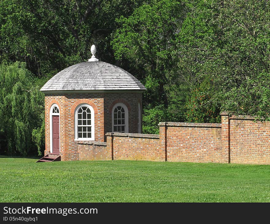 Enclosed brick gazebo attached to a brick wall, with green lawn in front and trees in the background. Enclosed brick gazebo attached to a brick wall, with green lawn in front and trees in the background.