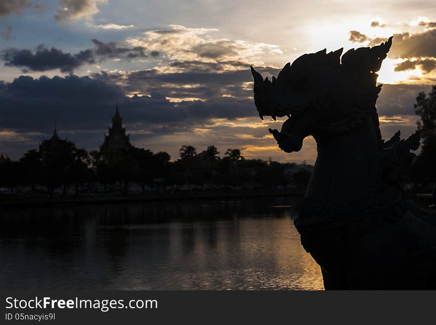 Silhouette lion carved in sunset sky with temple and tree reflection