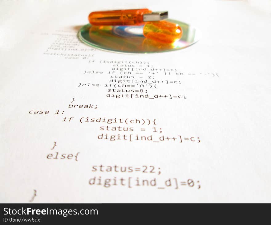 Orange flash drive and mini cd disc over a white sheet of paper with source code. Orange flash drive and mini cd disc over a white sheet of paper with source code.