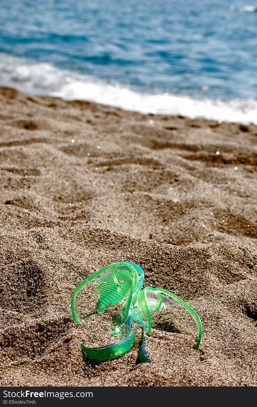 Green flipflop on a beach covered by sand and the sea in the background. Green flipflop on a beach covered by sand and the sea in the background