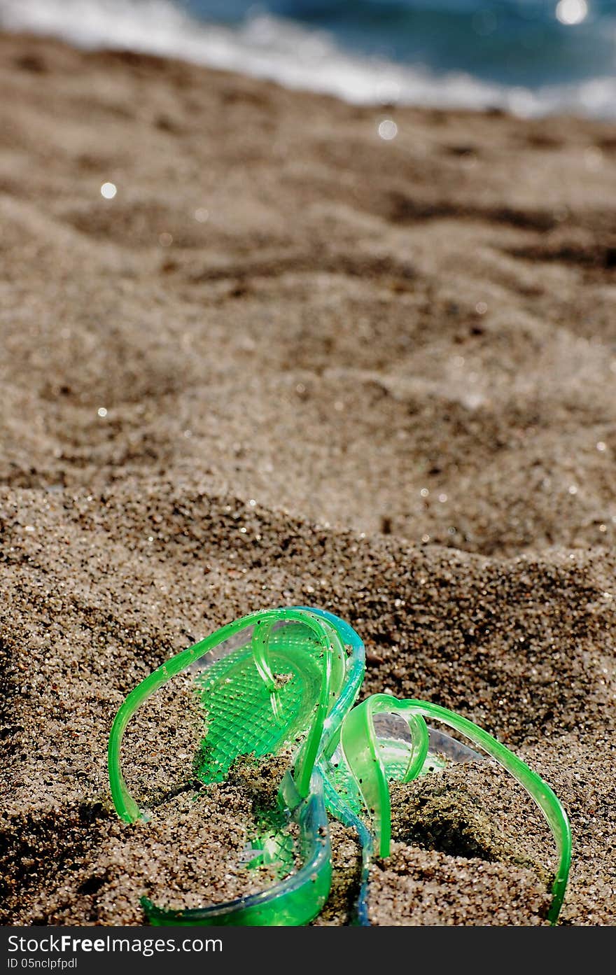 Green flipflop on a beach covered by sand and the sea in the background. Green flipflop on a beach covered by sand and the sea in the background