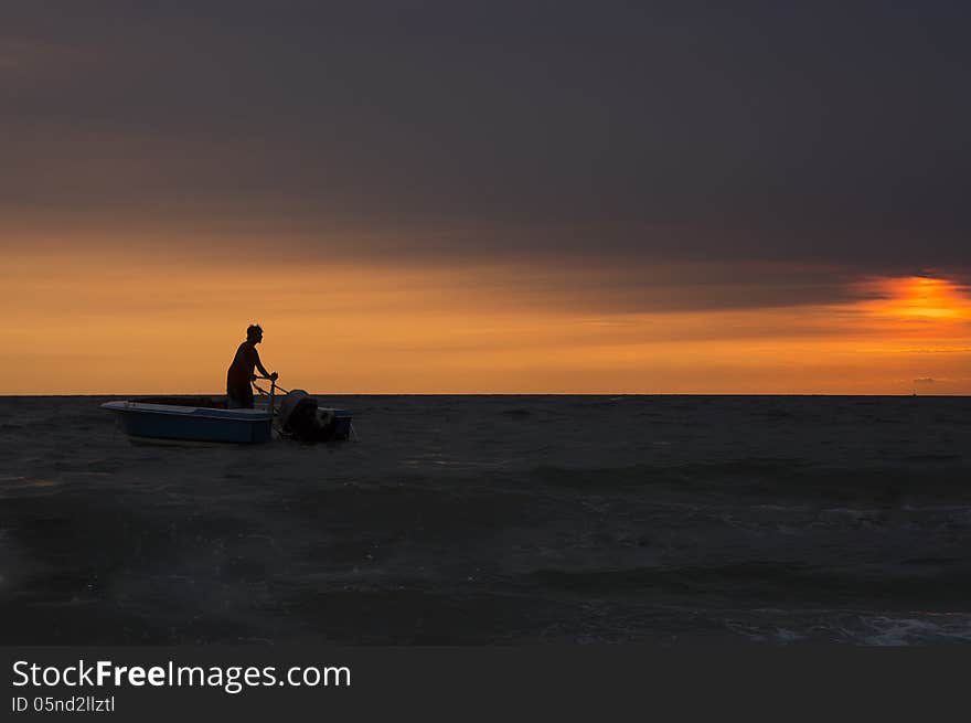 Fisherman anchoring his boat at beach during sunset. Fisherman anchoring his boat at beach during sunset