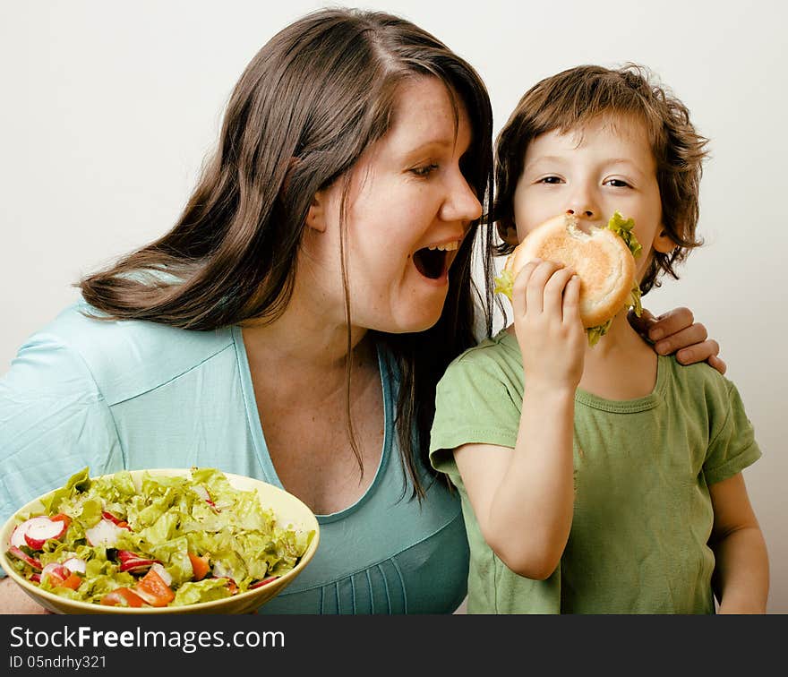 Fat women holding salad and little cute boy with hamburger on white background. Fat women holding salad and little cute boy with hamburger on white background