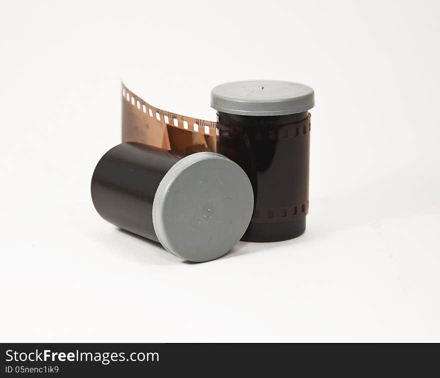 Two black and grey film canisters and a negative against a white background