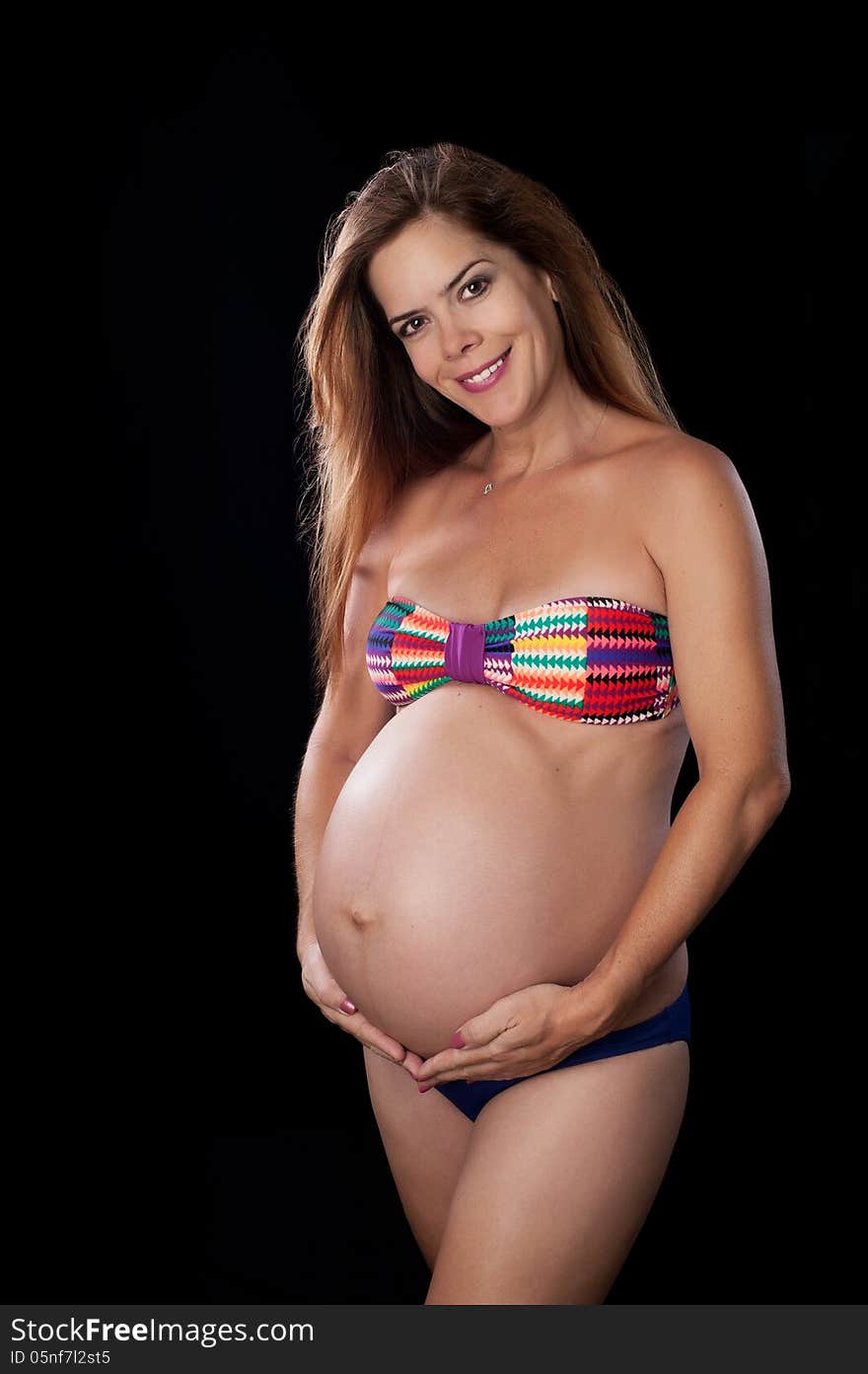 An attractive and physically fit pregnant woman wearing a bikini swimming suit. She is on a black background and smiling at the camera. An attractive and physically fit pregnant woman wearing a bikini swimming suit. She is on a black background and smiling at the camera.