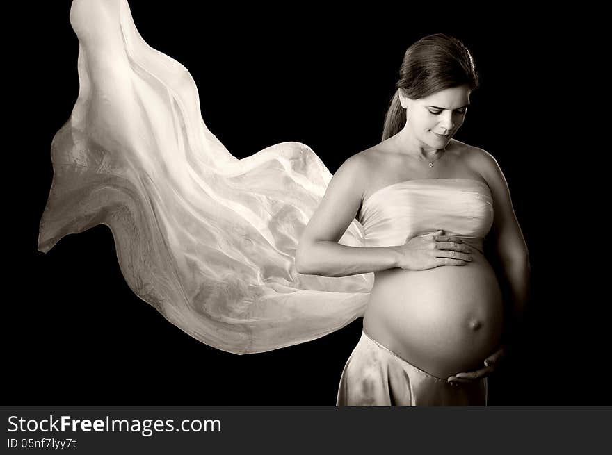 A black and white portrait of a beautiful pregnant woman looking down at her belly and smiling. She has a flowing white silk veil doubling as a bandeau top. A black and white portrait of a beautiful pregnant woman looking down at her belly and smiling. She has a flowing white silk veil doubling as a bandeau top.