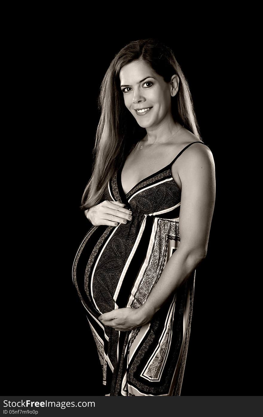 Black and white portrait of a beautiful pregnant woman. She is smiling, looking at the camera and holding her belly. Isolated on a black background.