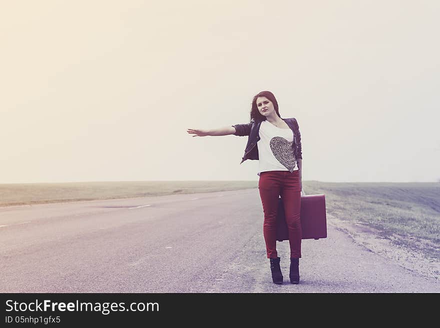 Girl standing on road with suitcase votes and looks for fellow traveler