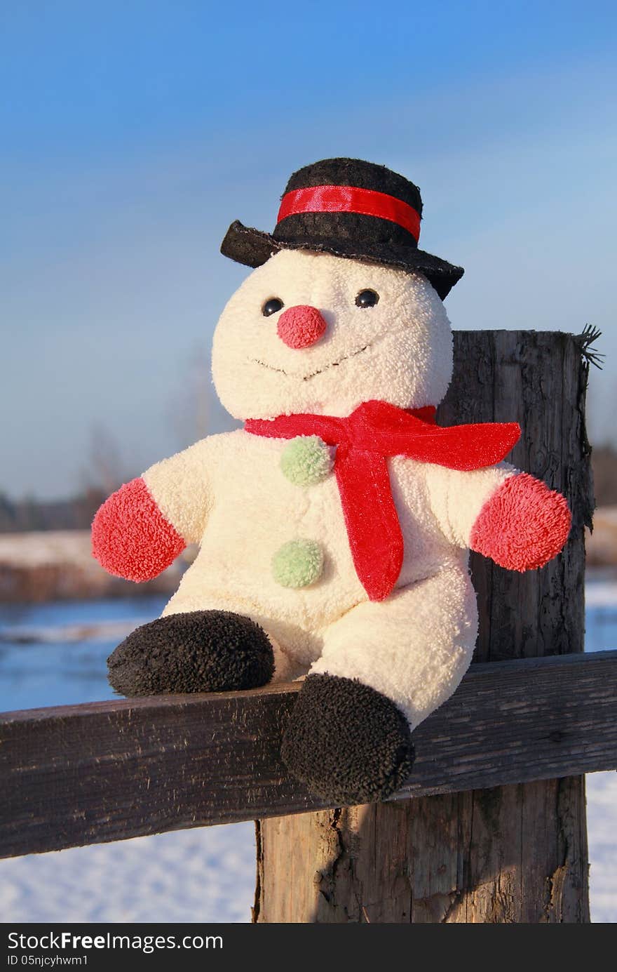 Toy snowman sitting on a wooden fence outdoors in winter. Toy snowman sitting on a wooden fence outdoors in winter