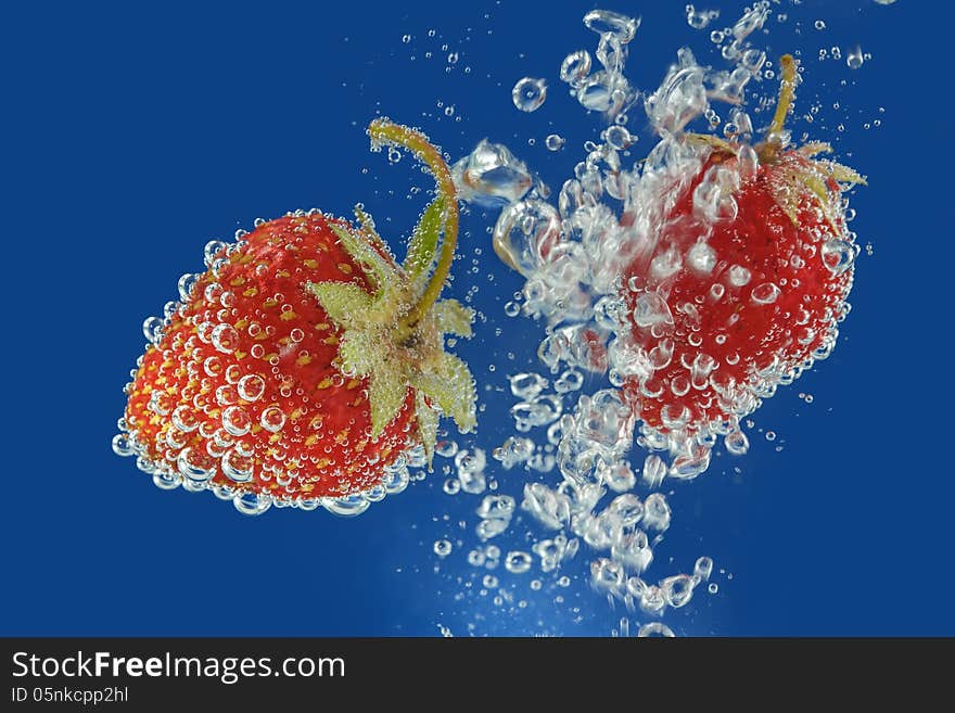 Splashes of water surrounding a fresh strawberry on a blue background