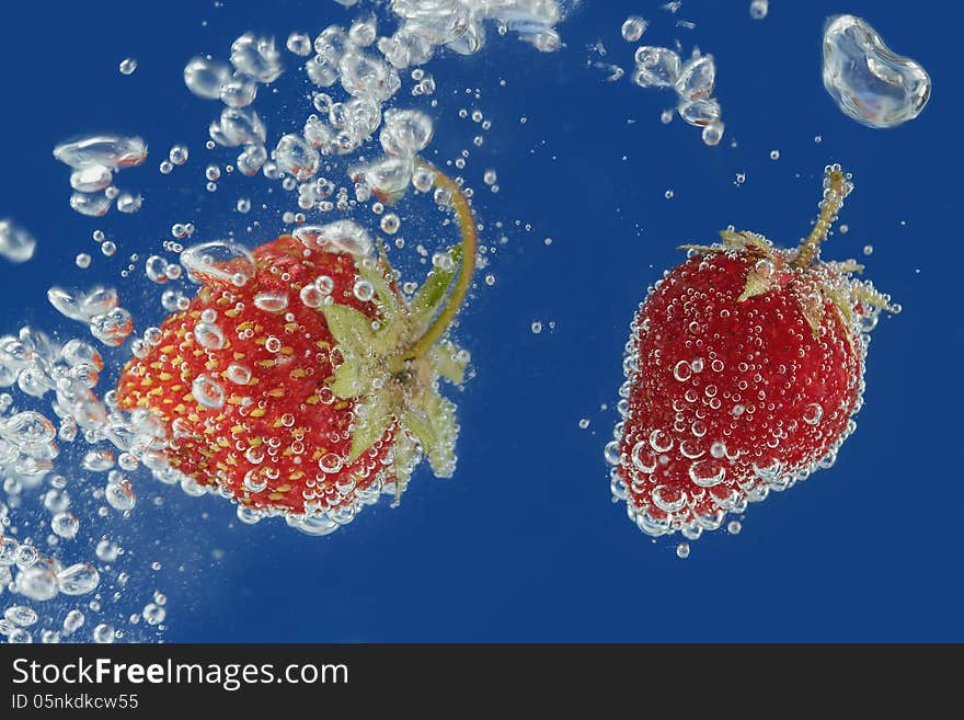 Splashes of water surrounding a fresh strawberry on a blue background