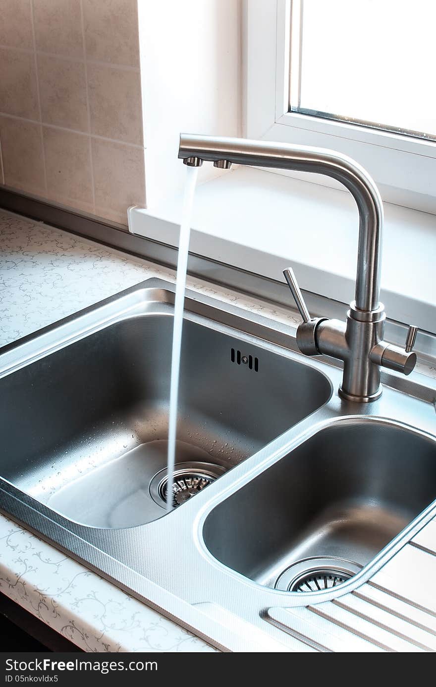 A stainless steel kitchen faucet includes a sink, water flows from the tap.